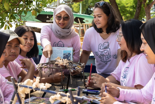 A group assembles coral frames at an outdoor reef-restoration workshop, guided by a facilitator.